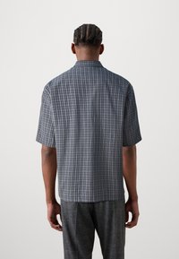 Short-sleeved shirt in dark gray and blue checkered pattern, relaxed fit with a button-down collar. Lightweight fabric, smooth texture.