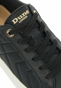 Black leather sneaker with quilted design, textured laces, and metallic eyelets. Features a white rubber sole and gold branding.