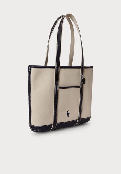 Béžová plátená taška s námorníckymi akcentmi, vybavená dvoma dlhými rúčkami a predným vreckom. Na prednej strane vyšívané logo.