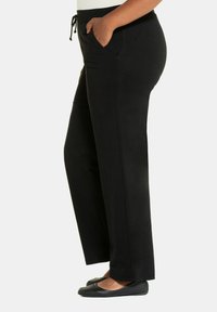 Pantaloni neri a tubino realizzati in tessuto morbido, dotati di vita regolabile con cordino e tasche laterali. Design a gamba dritta con una finitura liscia e opaca.