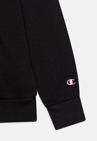 Manica di un felpa nera realizzata in tessuto misto cotone, con polsino a costine e un piccolo logo ricamato in blu, rosso e bianco.