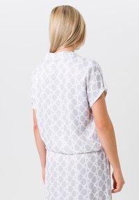 Lichte, kortärmige blouse van doorschijnende witte stof met een cirkelpatroon. Beschikt over een kraag en een relaxed fit aan de achterkant.