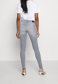 Grå skinny jeans med hög midja, som har bakfickor och en snygg, slät textur. Kombinerat med en enkel vit t-shirt och vita klackar.