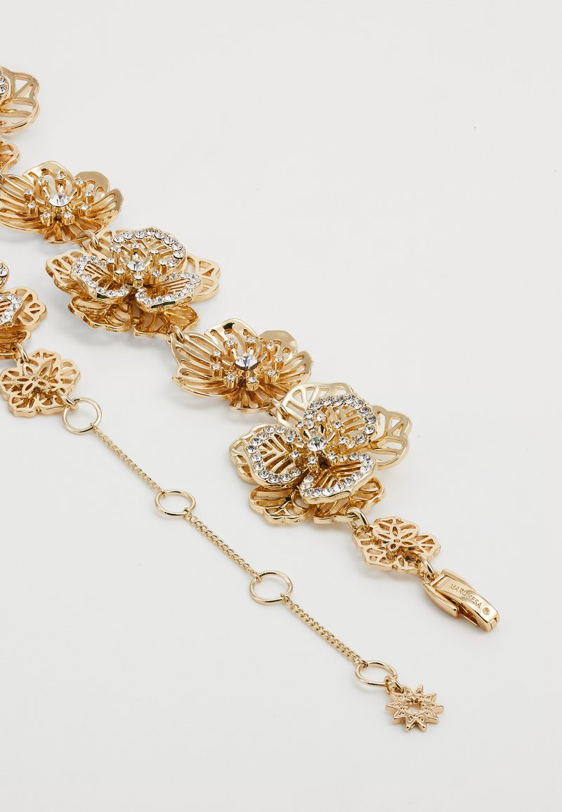 Armbånd i gulltone med intrikate blomsterdesigns, dekorert med klare rhinestones. Inkluderer en krokfeste og forlengelseskjede.