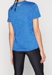 Blue, short-sleeve athletic shirt with a heathered texture and a logo on the back, paired with black leggings.