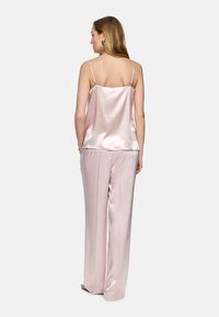 Pajama set featuring a pink satin camisole with adjustable straps and loose-fitting satin trousers, both with a smooth, shiny texture.