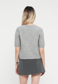 Pull gris à manches courtes en tricot doux, avec un col rond et un ourlet côtelé. Porté par-dessus une jupe grise avec des liens latéraux.