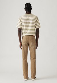 Camiseta de manga corta a rayas beige y blanca combinada con jeans de pierna recta en marrón claro. Parche de cuero visible en la pretina y los bolsillos traseros.