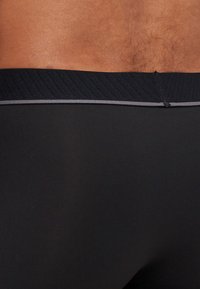 Schwarze Stoff-Boxershorts mit einem gerippten Bund in Grau. Glatte Textur mit einer figurbetonten Passform.