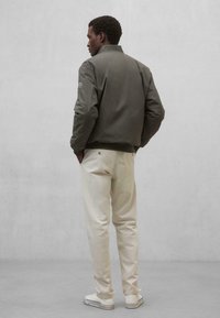 Chaqueta bomber verde oliva con cuello, puños y cinturilla acanalados. Pantalones beiges de corte slim y con un detalle mínimo. Zapatillas blancas.