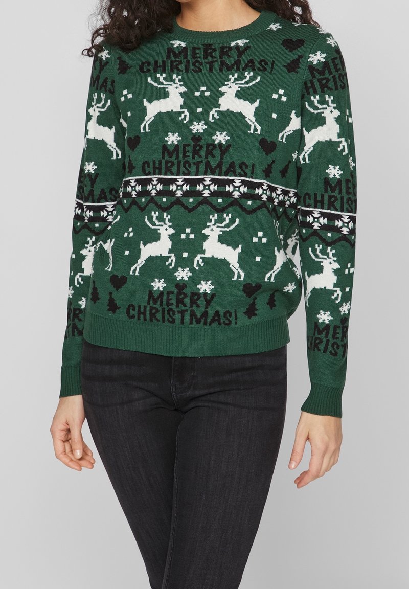 Grüner Weihnachtspullover aus Strickstoff, mit weißen Rentieren, Schneeflocken und dem Text "Frohe Weihnachten!" in schwarz-weißen Mustern.