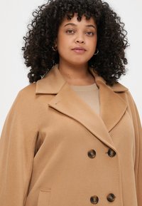 Παλτό μείγματος καμήλας με σχέδιο διπλής σειράς κουμπιών, μεγάλα πέτα και σκούρα κουμπιά. Διαθέτει μαλακή υφή και πλαϊνές τσέπες.