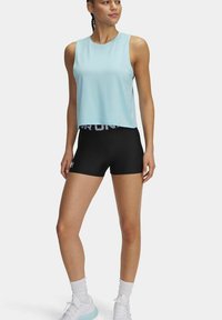 Lichtblauw mouwloos sporttopje gecombineerd met zwarte high-waist shorts met een witte "STRONG" band. Het model draagt witte sokken en sneakers.