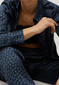 Persona in abito blu navy con motivo floreale e pantaloni coordinati, giacca aperta che mostra un top corto nero sottostante.