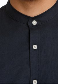 Camisa de color azul marino con cuello y tapeta de botones, que presenta botones blancos, una textura suave y un diseño ajustado alrededor del cuello.