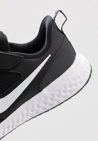 Zapatilla deportiva negra con un diseño elegante, parte superior de malla, logotipo de Nike en blanco y suela de goma texturizada. Presenta una lengüeta en el talón.