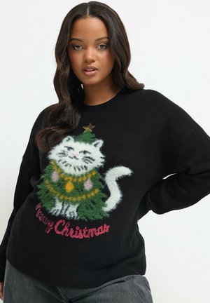 Femme portant un pull noir avec un chat blanc duveteux déguisé en sapin de Noël et texte en rouge "Merry Christmas".