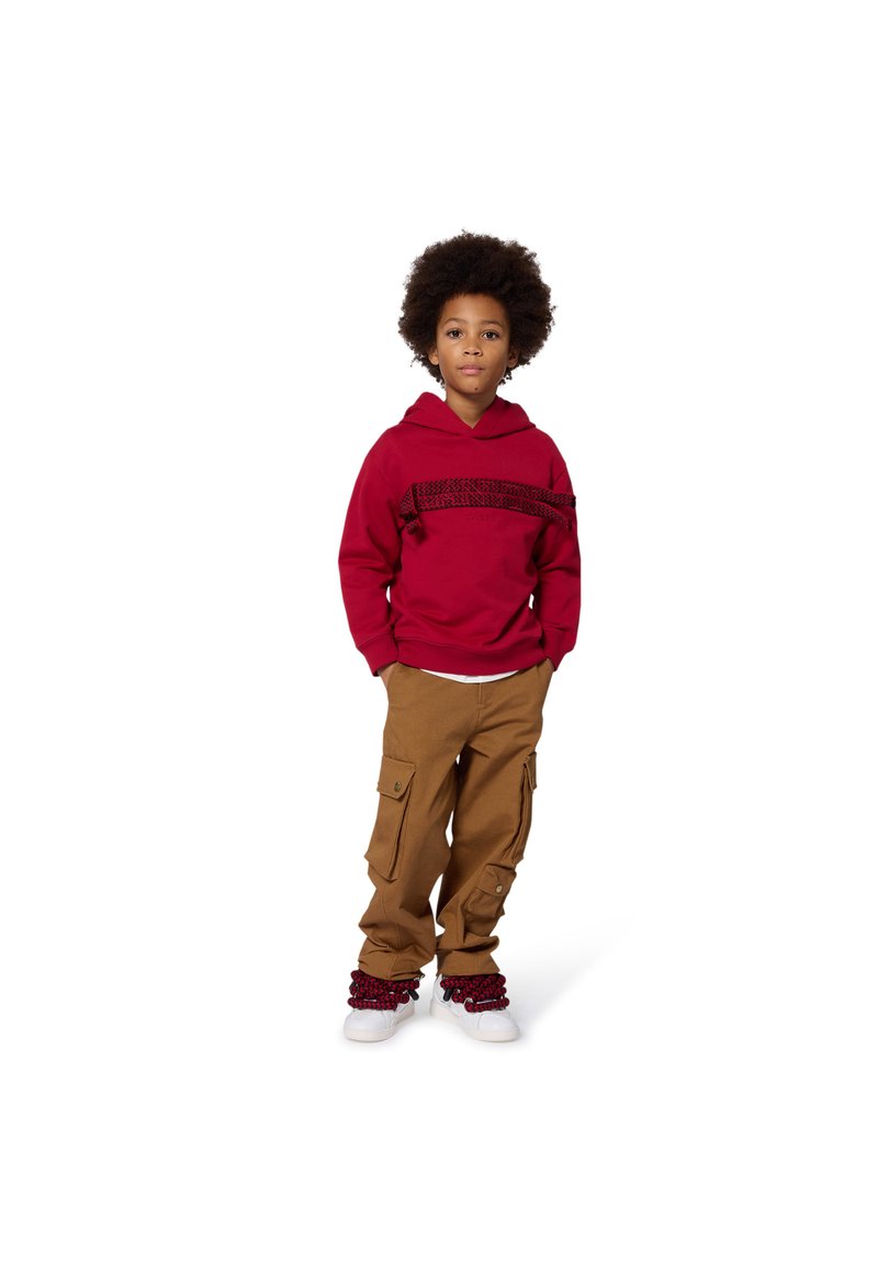 Czerwona bluza z kapturem z teksturowanym poziomym wzorem, połączona z beżowymi spodniami typu cargo z kieszeniami po bokach oraz białymi trampkami z czerwonymi akcentami.