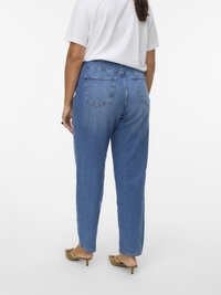 Modré džíny s vysokým pasem a rovnými nohavicemi, s kapsami na zadní straně a světlejším vyblednutím. Kombinovány s bílým tričkem a zelenými podpatky.