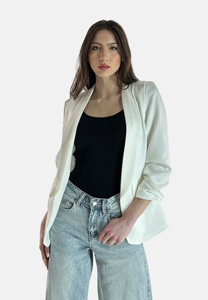 Witte blazer met een gladde stof en open voorkant, gedragen over een zwarte tanktop, gecombineerd met lichtblauwe wijde jeans.
