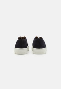 Marineblaue Wildledersneakers mit weißen Gummisohlen, abgerundeten Fersen und kontrastierenden braunen Akzenten an der Ferse. Minimalistisches Design, glatte Textur.