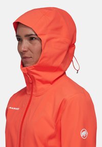Veste imperméable orange vif avec une capuche ajustée, fermeture éclair à l'avant et logo sur la poitrine et la manche. Texture lisse, tissu léger.