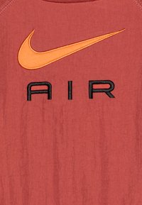 Red fabric T-shirt featuring a large orange Nike swoosh logo and black "AIR" text, with a textured finish and contrasting neckline.