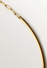 La cadena de metal en tono dorado presenta eslabones alargados y un segmento de barra delgada, exhibiendo una textura brillante y suave con un sutil acabado mate.