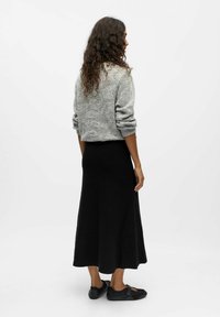 Grauer Strickpullover mit strukturiertem Muster, kombiniert mit einem schwarzen, knöchellangen, figurbetonten Rock und schwarzen Schuhen mit Riemen-Design.