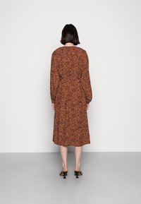 Abito midi con stampa leopardata marrone, maniche lunghe, vita aderente e fondo a strati. Indossato con mule nere con tacco, mostrato da dietro.