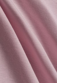 Pink cotton fabric with a ribbed texture, showing soft creases and folds. The material appears smooth and lightweight.