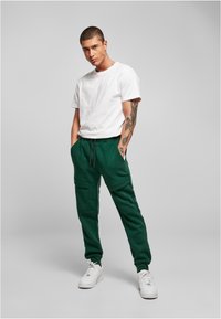 Witte T-shirt met korte mouwen in combinatie met donkergroene joggingbroek met zijzakken en een trekkoord in de taille. Gemaakt met witte sneakers.