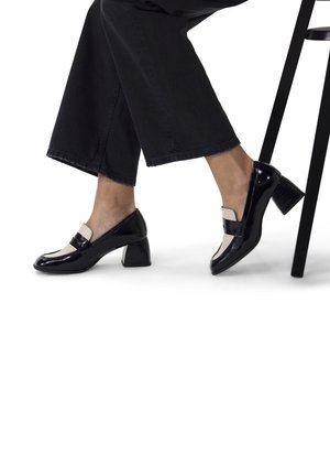 Zwarte lakleren pumps met een ronde neus en een contrasterende witte band over de wreef; blokhak; gladde textuur.