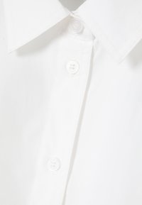 Camicia bianca con colletto classico, in tessuto liscio e quattro bottoni bianchi circolari lungo la patta.