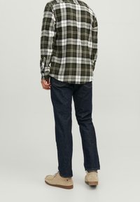 Camicia a quadri verde e bianca, in flanella, abbinata a jeans blu scuro e scarpe beige. Presenta polsini con bottoni e un orlo arrotondato.