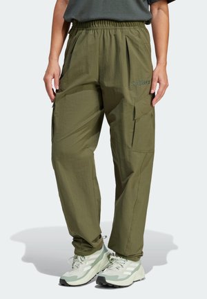 Personne portant un pantalon cargo vert olive avec une taille élastique et des poches latérales, associé à des chaussures de sport blanches et vert clair.