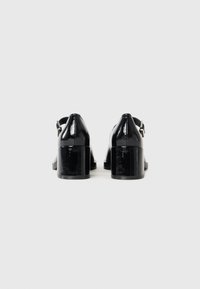 Bottines à talons en cuir verni noir avec un bout rond et un talon bloc épais. Elles possèdent une sangle à la cheville avec une boucle en argent pour un ajustement sécurisé.