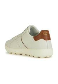 Sneaker bianco in pelle con un accento in pelle marrone sul tallone, dettagli cuciti e una suola bianca spessa. Presenta un design minimalista e una forma rotonda.