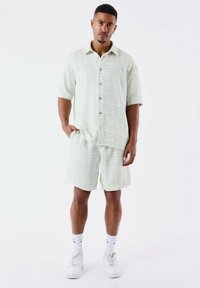Korte mouwen, knoopshirt en bijpassende shorts in een lichtgroen geruit patroon, gemaakt van textuurstof met een relaxte fit. Witte sneakers zichtbaar.