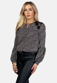 Czarna i biała bluzka z dekoltem w kształcie łezki oraz bufkami, ozdobiona koronkowym akcentem w kwiaty i kropeczkowym wzorem. Połączona z czarnymi spodniami.
