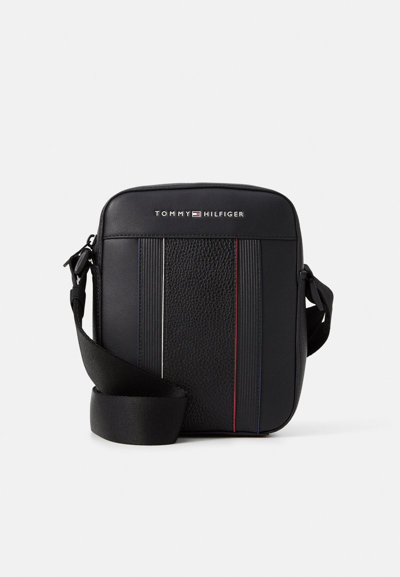 Černá kožená crossbody taška s texturovaným předním dílem, jemnými pruhy v červené a modré barvě a nastavitelným černým popruhem. Na tašce je zobrazeno logo Tommy Hilfiger.