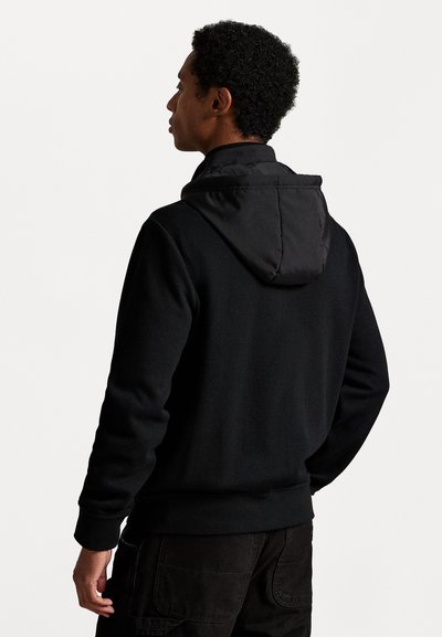 Μαύρη κουκούλα με αντίθετη μαύρη κουκούλα. Το ύφασμα φαίνεται υφασμένο και μαλακό, με σχέδιο που εφαρμόζει καλά και ραμμένα μανίκια και ζώνη.