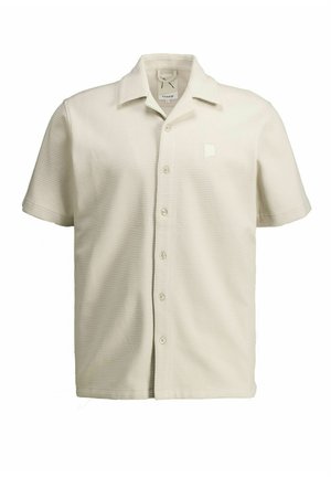 Chemise boutonnée à manches courtes de couleur crème avec tissu texturé et col pointu, présentée sur un fond blanc.