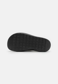 Suela de zapato de goma negra con un patrón de rejilla texturizado, con una pequeña impresión de logo. Bordes suaves con una ligera curvatura en el talón.