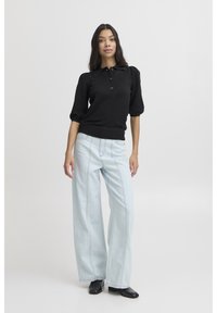 Juoda trumpomis rankovėmis polo palaidinė su apykakle, derinama su šviesiai mėlynomis plačiomis džinsų kelnėmis su priekinėmis siuvimo detalėmis ir juodais batais.