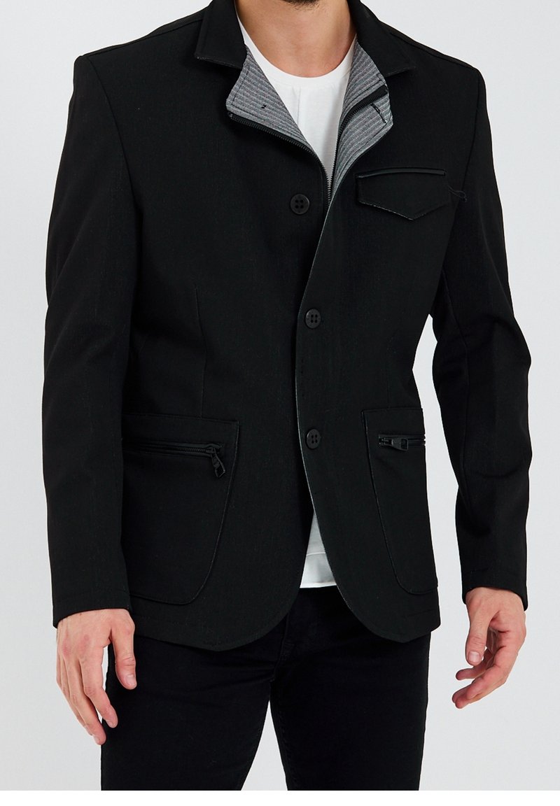 Czarna kurtka o fakturowanym wykończeniu, z szarą podszewką z kołnierzem, guzikiem z przodu oraz zamykanymi na zamek błyskawiczny bocznymi kieszeniami. Dopasowany krój o eleganckim fasonie.