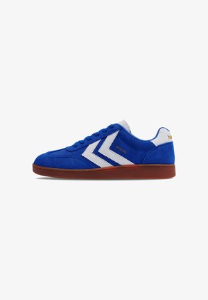 Blue suede sneaker with white stripes, rubber sole, rounded toe, and textured accents on the heel. Features flat laces and logo detail.