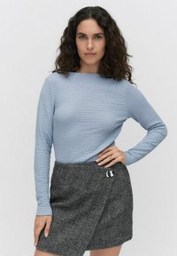Ljust blå strukturerad långärmad topp i kombination med en svart och vit herringbonekjol, med en dekorativ brosch på midjan.