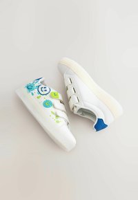 Pair of white sneakers with blue heel accents, velcro straps, and colorful paint splatter and emoji designs on one shoe.