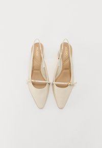 Beige slingback hæler med spids tå, justerbar rem og guldspænde detalje. Glat materiale og polstret indersål for komfort.